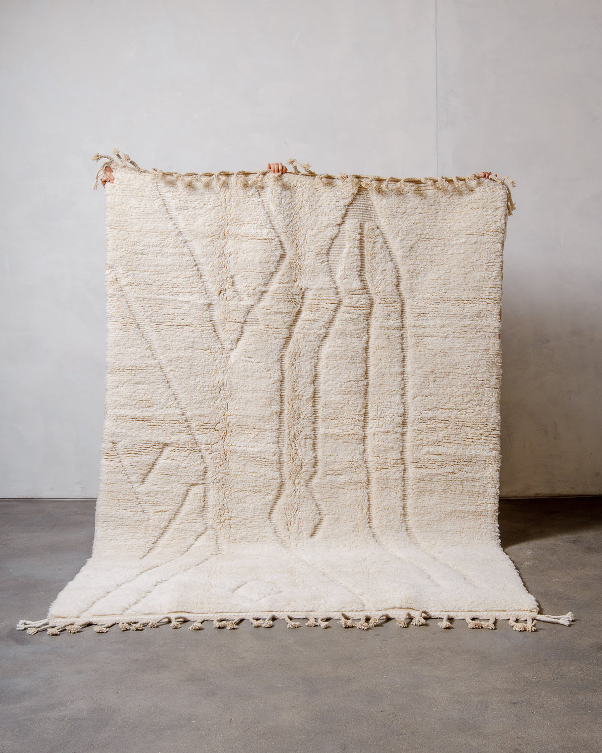 Berberlin Beniourain Rug made of cream wool being held up in front of a white wall.